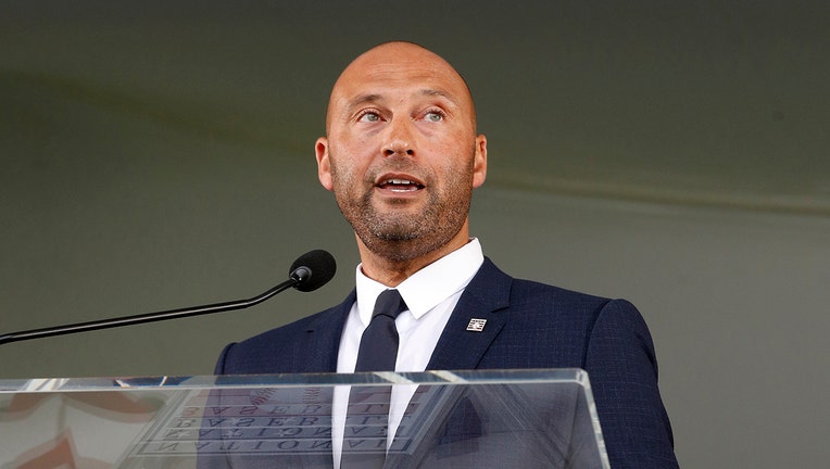 Derek Jeter, wearing a dark blue suit, speaks into a microphone at a lectern
