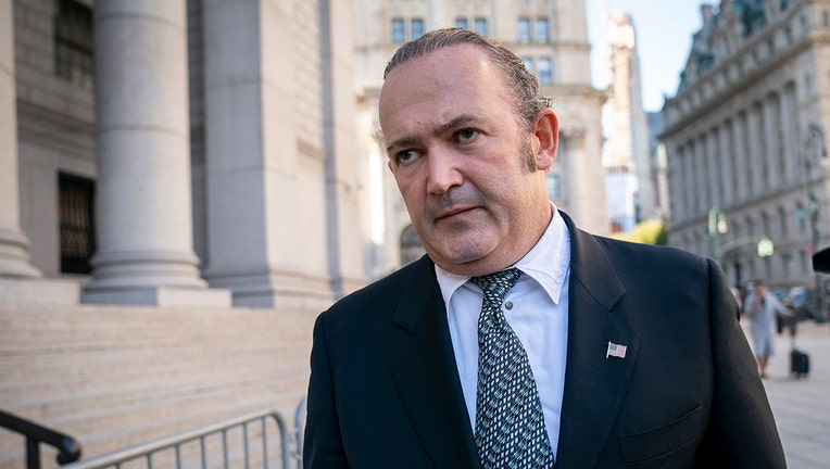 Man in a dark suit walks outside a courthouse