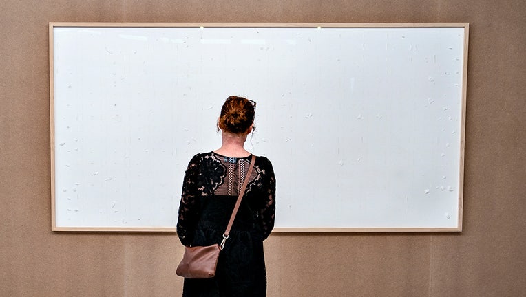 A woman stands in front of an empty frame hung up at the Kunsten Museum in Aalborg, Denmark, on September 28 2021. - The Danish museum loaned an artist $84,000 in cash to recreate old artworks of his using the banknotes, but the boxes he sent only contained blank canvasses and a new title: "Take the Money and Run". Danish artist Jens Haaning had done just that, pocketing the money the Kunsten Museum in the western city of Aalborg had loaned him to reproduce two works that used Danish kroner and euros to represent the annual salary in Denmark and Austria. (Photo by HENNING BAGGER/Ritzau Scanpix/AFP via Getty Images)