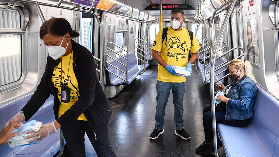 MTA workers wearing white masks and yellow shirts hand out masks to riders in an almost-empty subway car