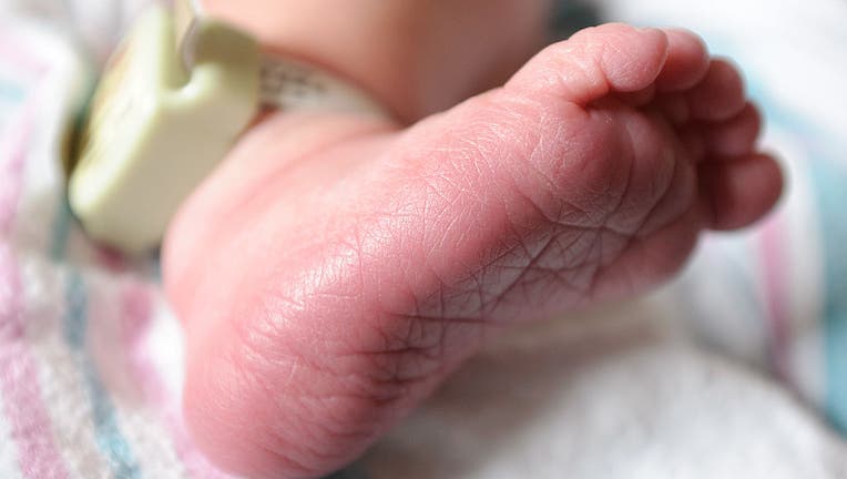 A baby's right foot with hospital bracelet and baby blanket.