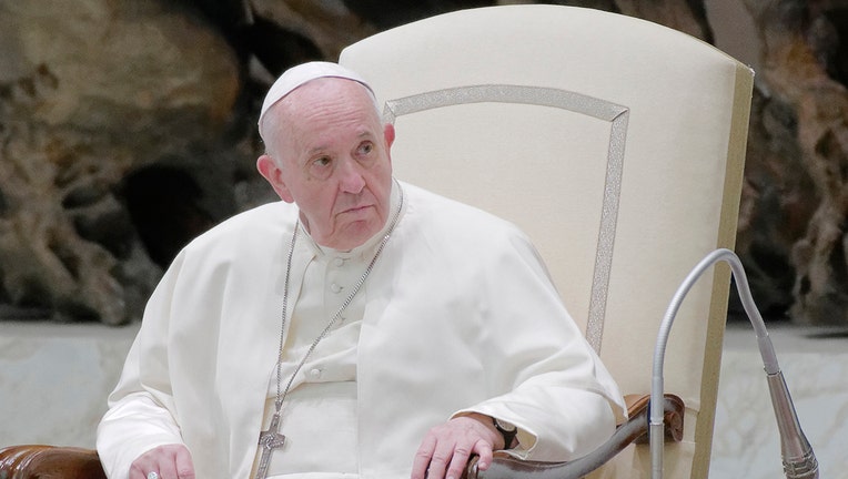 Pope Francis wearing white vestments and skullcap sits in a large chair