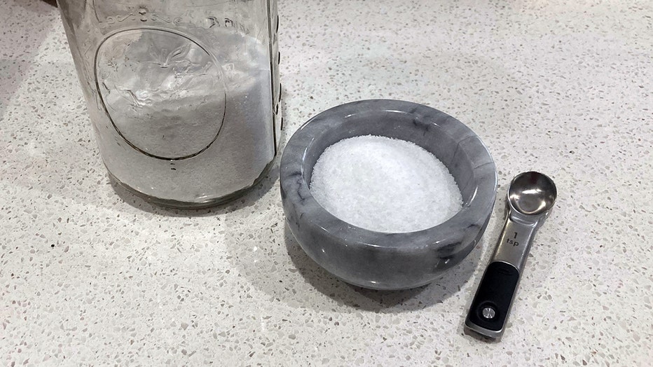 A mason jar and a gray ceramic bowl containing kosher salt; a 1 teaspoon measuring spoon