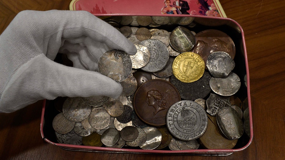 A gloved hand holds a rare coin above a box of coins
