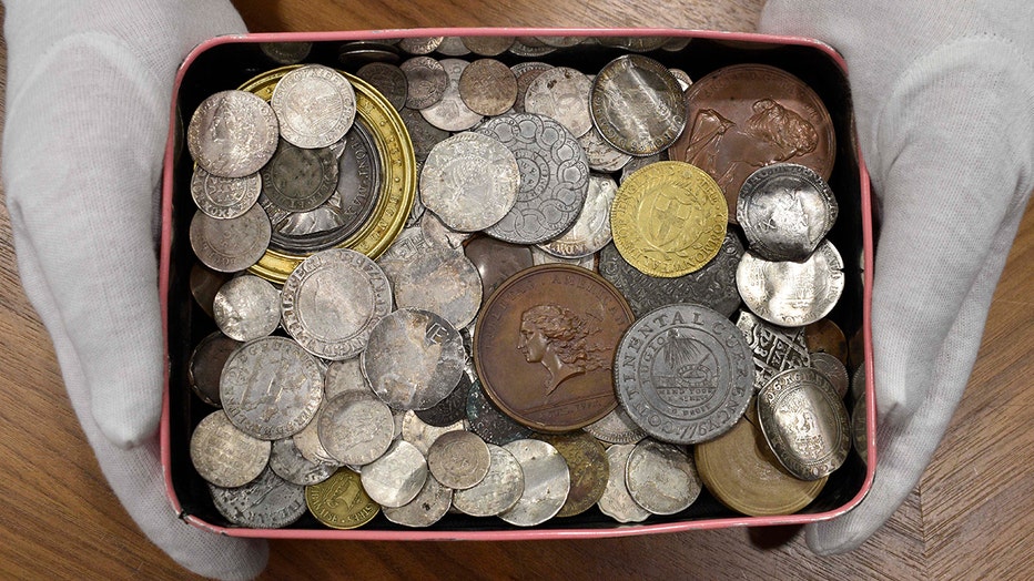 Gloved hands hold a metal box of rare coins