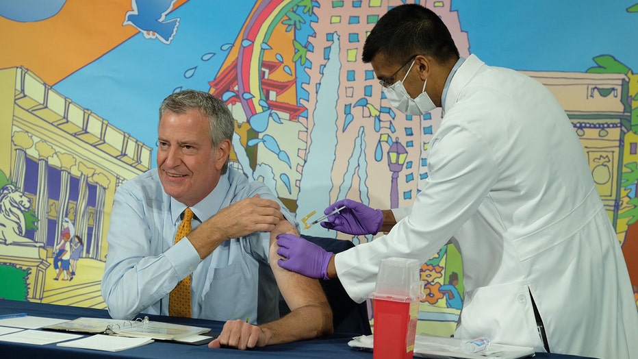 health commissioner in a white coat gives vaccine to mayor