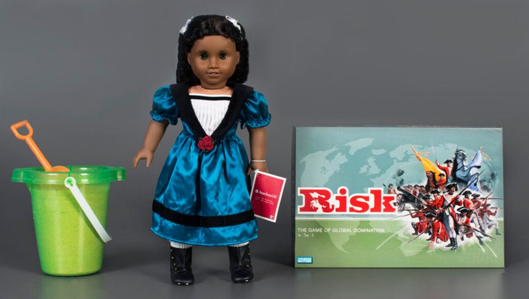 Left to right: a green plastic pail containing sand, an American Girl Doll, and the board game Risk