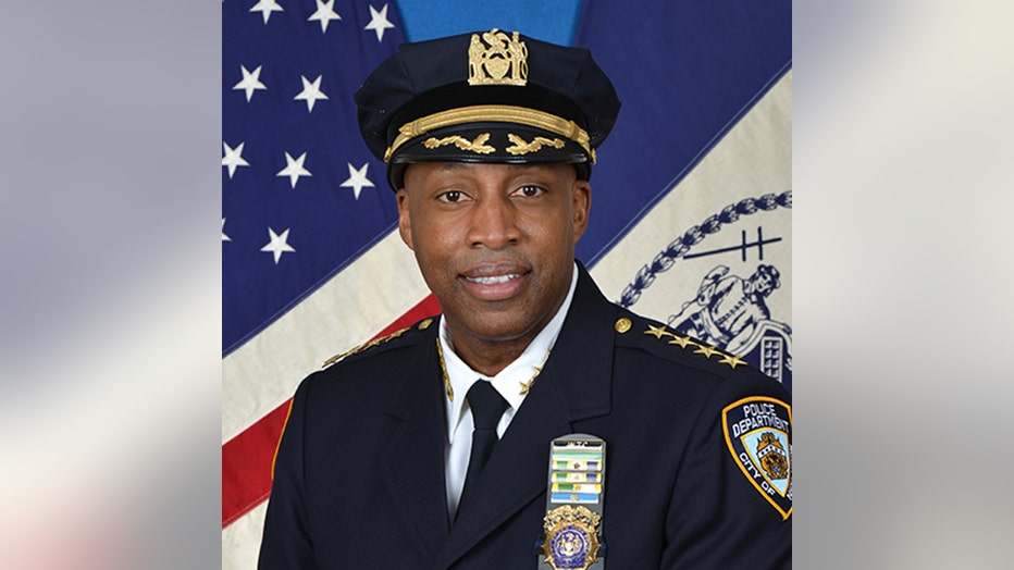 Head and shoulders photo of Chief Rodney Harrison wearing a navy blue police uniform, tie and hat; white shirt; gold shield, 4 stars in front of US and NYC flags