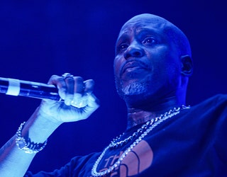Closeup of DMX on stage holding a microphone; he is wearing large necklaces, a bracelet and a dark shirt