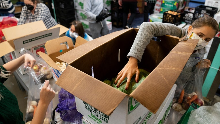 A volunteer wearing a mask places produce inside a cardboard box at a food pantry