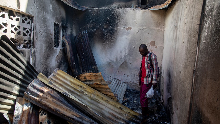 A resident looks at collapsed tin roof inside a burned-out home