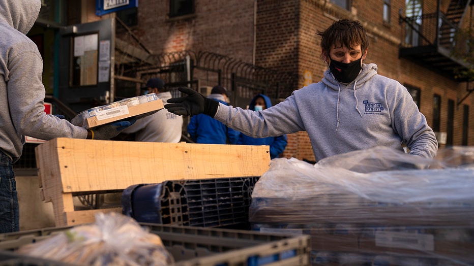 A volunteer wearing a mask, gloves and a sweatshirt unloads cases of canned foods