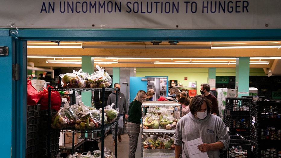 Volunteers wearing masks pack food; several bags of produce sit on shelves
