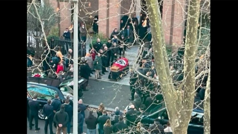 A picture made available by the Italian online news portal Open, showing people gathered around a swastika-covered casket outside the St. Lucia church, in Rome, Monday, Jan. 10, 2022. The Catholic Church in Rome on Tuesday, Jan. 11, 2022, strongly condemned as "offensive and unacceptable" a funeral procession outside a church in which the casket was draped in a Nazi flag and mourners gave the fascist salute. (Open Via APTV)