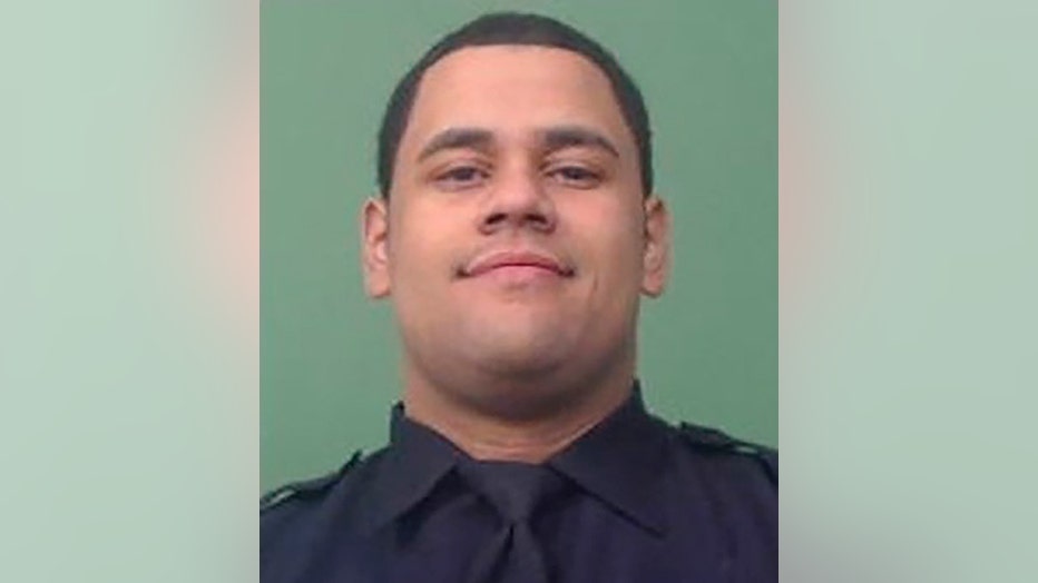 Closeup photo of Officer Wilbert Mora wearing a dark blue uniform shirt and tie; background is green