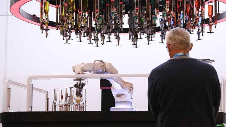 A man stands in front of a bar where an arm-like robot prepares a cocktail