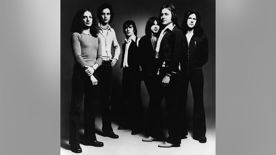 A shadowy, black-and-white group photo of the 6 members of the band Foreigner; they all have long hair