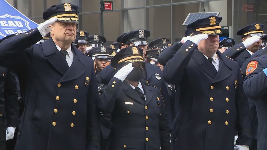 Several police officers in dark blue dress uniforms and white gloves saluting