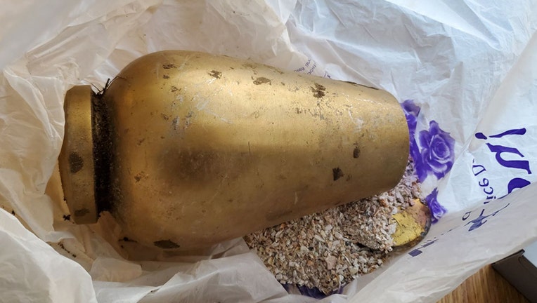 A gold pear-shaped urn lying on its side with ashes coming out