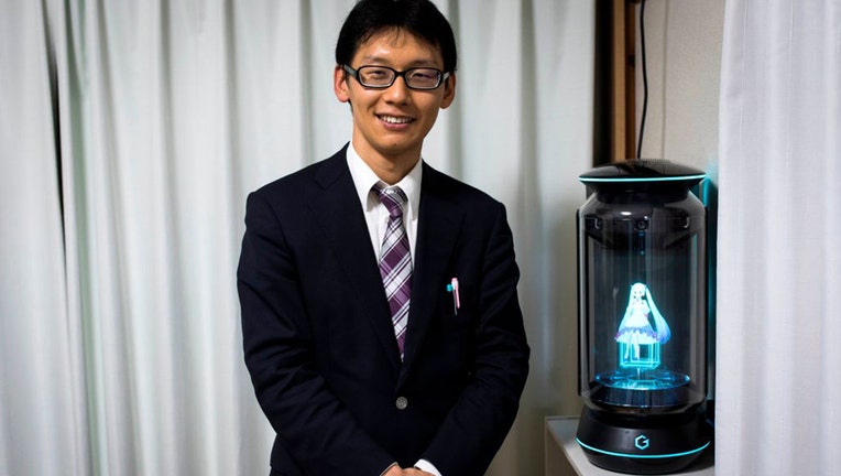 In this photograph taken on November 10, 2018 Japanese Akihiko Kondo poses next to a hologram of Japanese virtual reality singer Hatsune Miku at his apartment in Tokyo, a week after marrying her.