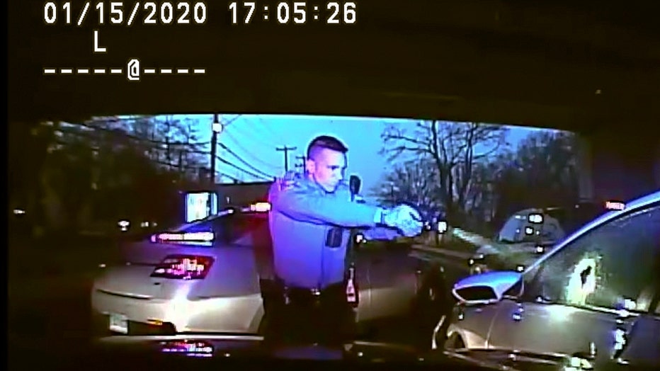 Dashboard cam image of a state trooper pointing a handgun at the driver's side window of a car; window has a large hole