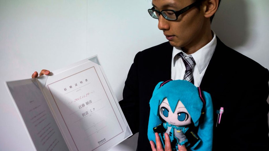 In this photograph taken on November 10, 2018 Japanese Akihiko Kondo poses with a doll of Japanese virtual reality singer Hatsune Miku, as he shows their marriage certificate, at his apartment in Tokyo, a week after marrying her. 