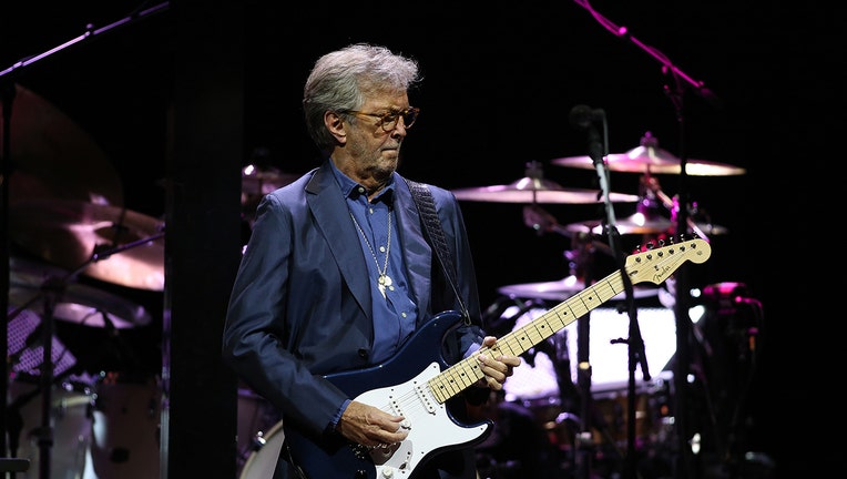 Eric Clapton plays guitar on stage; he wears a blue suit