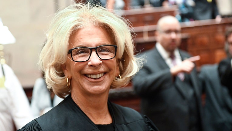 Judge Janet DiFiore smiles; she wears a black robe and black-rimmed glasses; she has light-colored hair