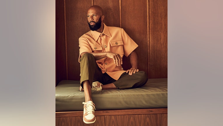 Actor Common sitting against wood paneling and lookin to his right; his right arm is propped up on his right knee
