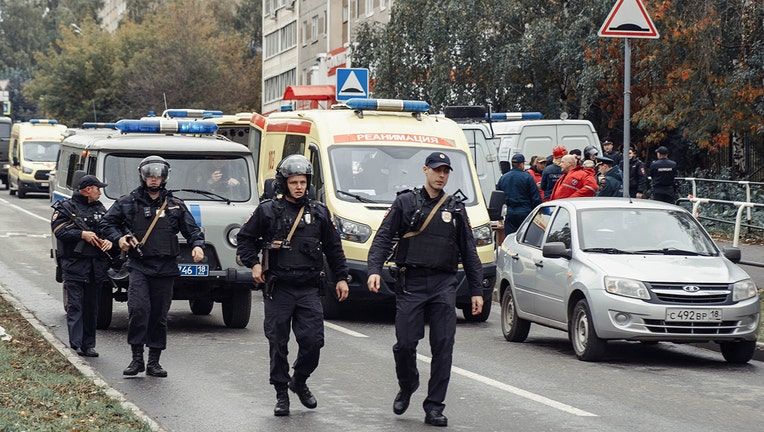 4 armed policemen walk past emergency vehicles outside a school