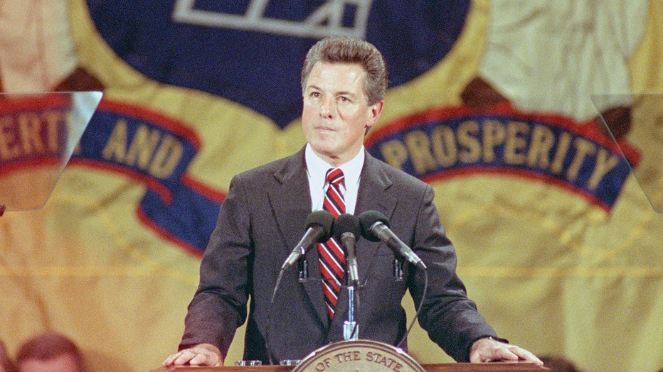 Gov. Jim Florio in a suit and tie stands in front of three microphones