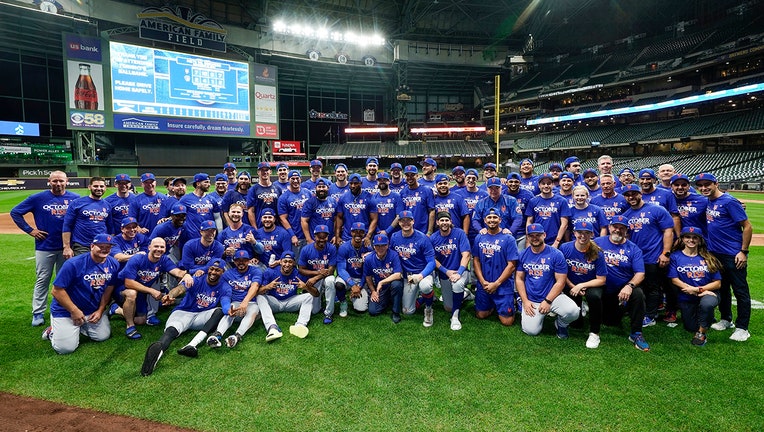 Dozens of Mets players in blue postseason T-shirts pose on the field to celebrate clinching a playoff spot