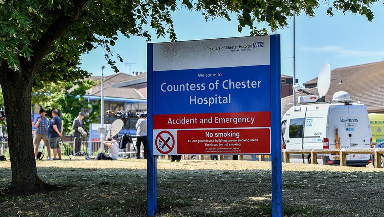 Large hospital sign on hospital property; media members, TV trucks
