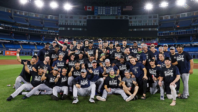 Dozens of Yankees players pose for a victory photo on a baseball field; they are wearing T-shirts that read "The East Is Ours"