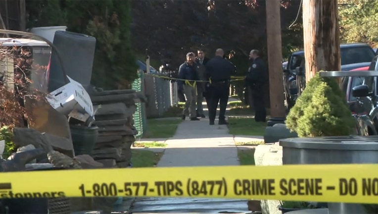 Crime scene tape stretched across a sidewalk; police seen in the distance outside a home