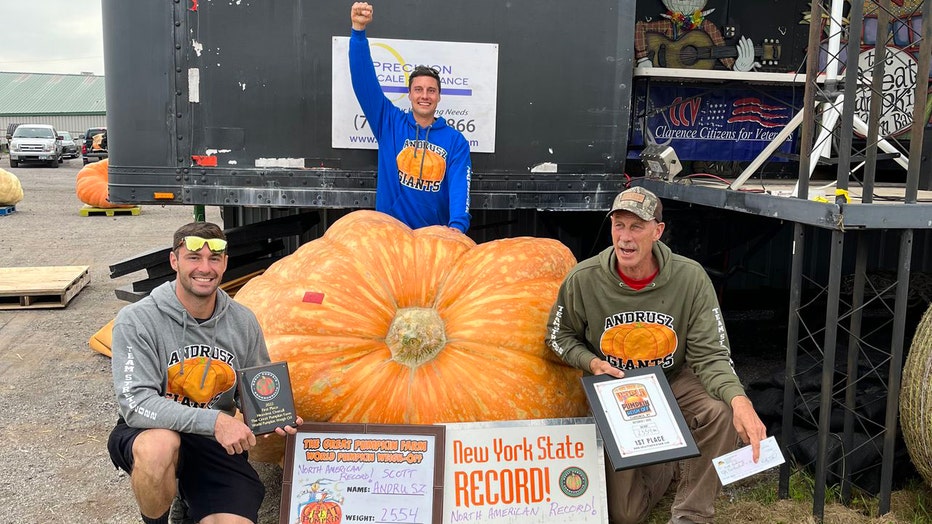 3 men pose with a massive orange pumpkin
