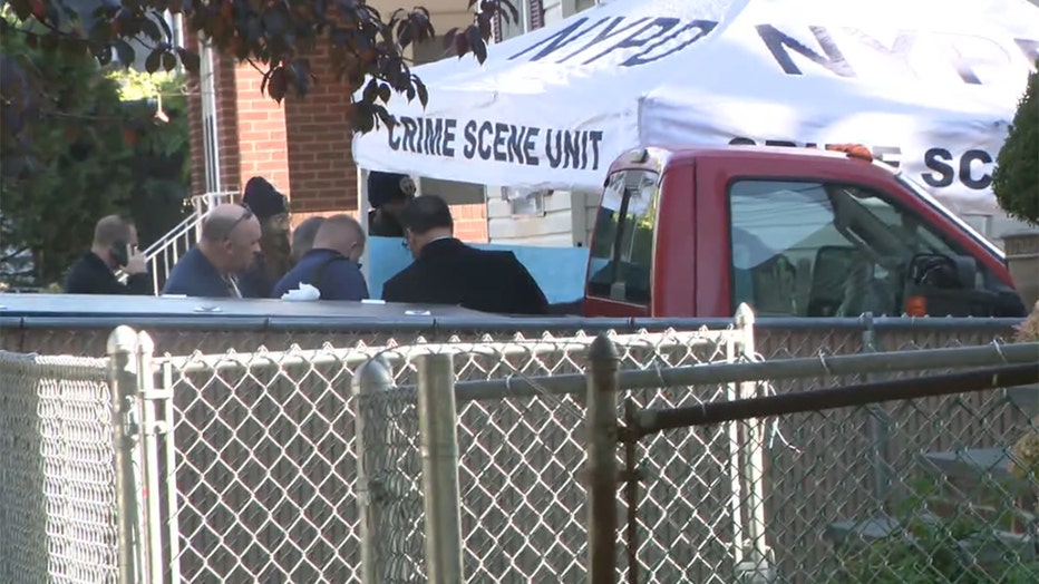 Cops stand near a white crime scene tent outside a house