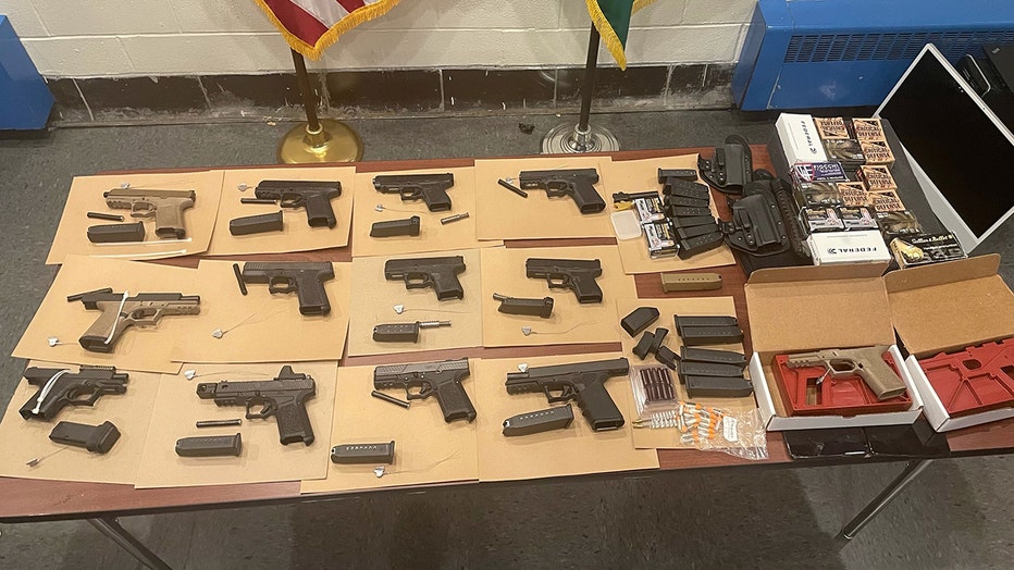 More than a dozen semiautomatic pistols and accessories displayed on a table