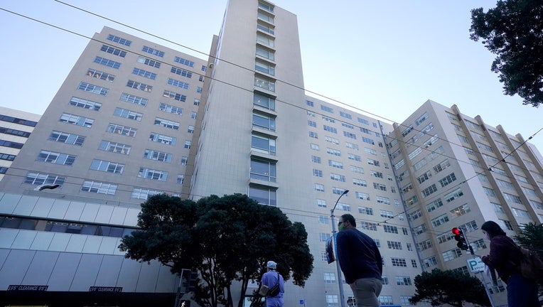 FILE - People cross the street in front of a University of California at San Francisco medical center in San Francisco on Nov. 30, 2020. A prominent California medical school has apologized for conducting unethical experimental medical treatments on 2,600 incarcerated men in the 1960s and 1970s. (AP Photo/Jeff Chiu, File)