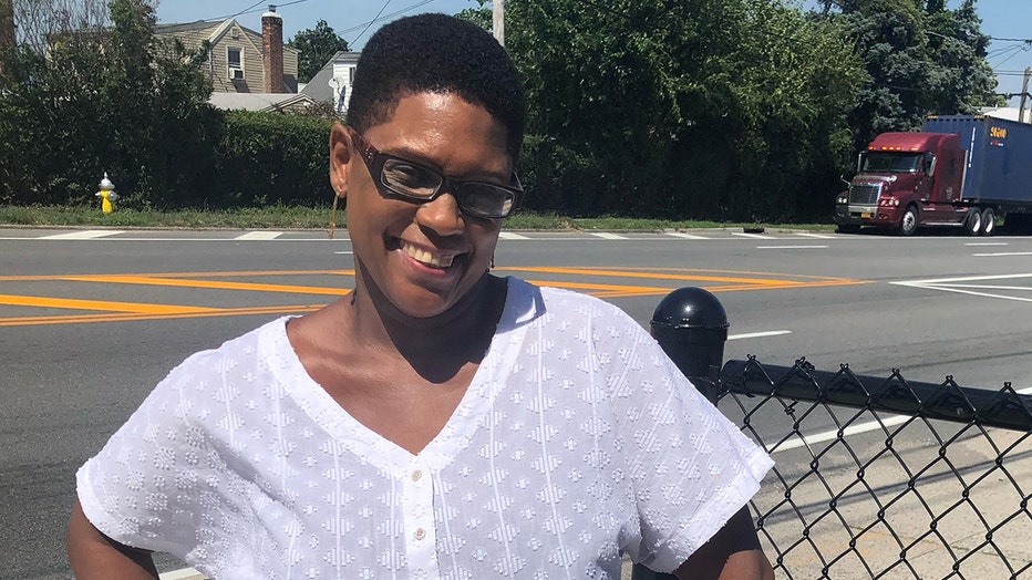 Woman smiling; she has short hair; she wears a white blouse, long earrings and glasses