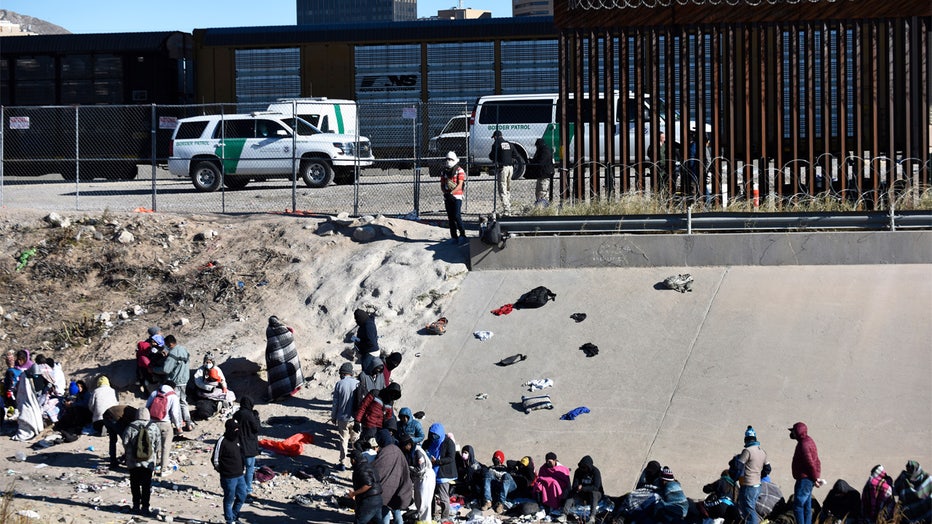 FILE - Migrants wait to cross the U.S.-Mexico border from Ciudad Juárez, Mexico, next to U.S. Border Patrol vehicles in El Paso, Texas, Wednesday, Dec. 14, 2022. A federal judge on Thursday temporarily blocked the Biden administration from ending a Trump-era policy requiring asylum-seekers to wait in Mexico for hearings in U.S. immigration court. (AP Photo/Christian Chavez, File)