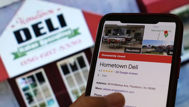 This illustration photo shows a person checking information online for the now permanently closed Paulsboro, New Jersey's Hometown Deli in front of a screen displaying the facade of the restaurant. (Photo by CHRIS DELMAS/AFP via Getty Images)