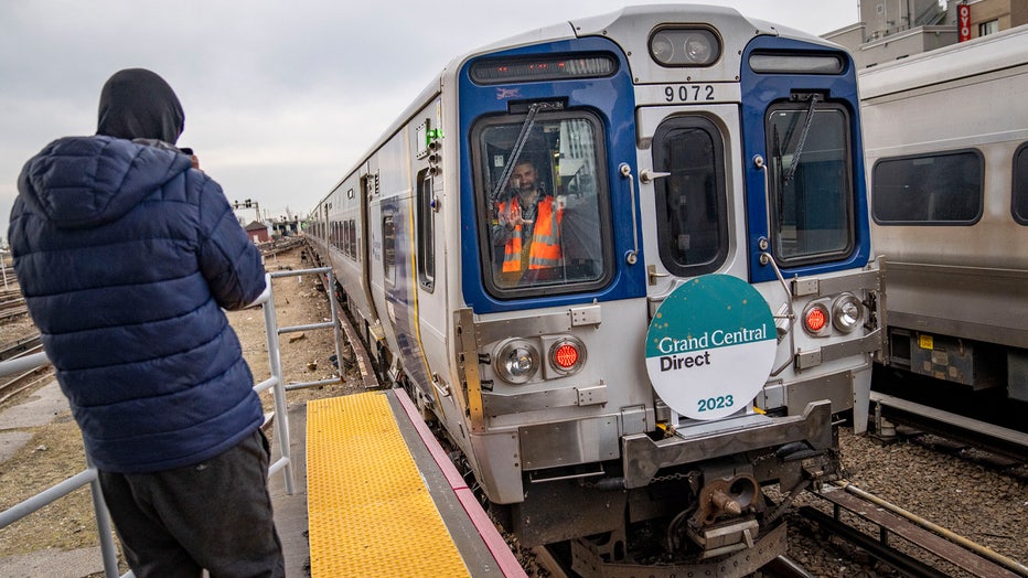 A rider in the rear conductor's booth waves to photographers on the platform after their Long Island Rail Road train departs for its inaugural trip from Jamaica station towards Grand Central Terminal, Wednesday, Jan. 25, 2023, in the Queens borough of New York. After years of delays and massive cost overruns, the railway project has begun shuttling its first passengers between Long Island to the latest addition to New York City's iconic Grand Central Terminal, dubbed Grand Central Madison because of its location along Madison Avenue.(AP Photo/John Minchillo)