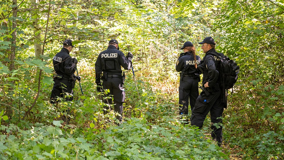 Police officers search a wooded area for clues and objects near which a female body was discovered in a passenger car on Aug. 17, 2022. (Photo by Peter Kneffel/picture alliance via Getty Images)