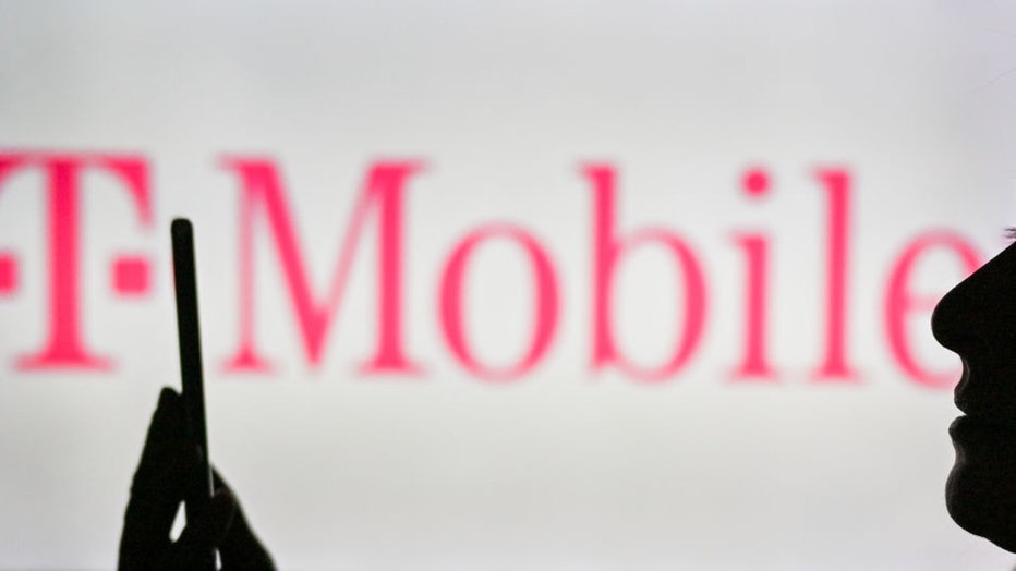 An image of a woman holding a cell phone in front of the T-Mobile logo displayed on a computer screen. On Tuesday, January 12, 2021, in Edmonton, Alberta, Canada. (Photo by Artur Widak/NurPhoto via Getty Images)