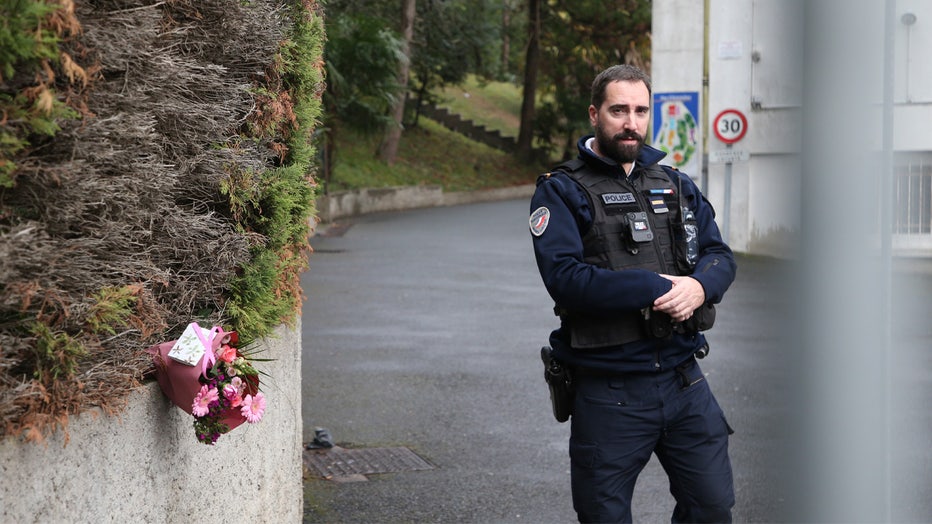 A police officer guards the entrance to a private Catholic school next to a bouquet of flowers after a teacher of Spanish has been stabbed to death by a high school student, Wednesday, Feb. 22, 2023 in Saint-Jean-de-Luz, southwestern France. The student has been arrested by police, the prosecutor of Bayonne said. (AP Photo/Bob Edme)