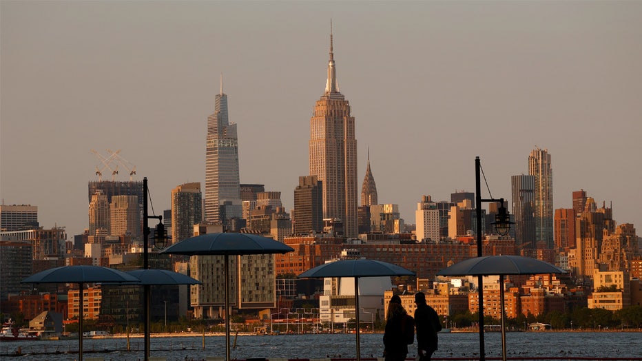 JERSEY CITY, NJ - MAY 18: The sun sets on the skyline of midtown Manhattan and the Empire State Building in New York City as people walk along the Hudson River on March 18, 2023, in Jersey City, New Jersey. (Photo by Gary Hershorn/Getty Images)
