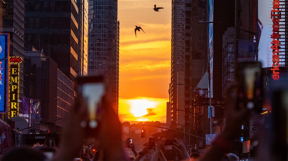 NEW YORK, NEW YORK - JULY 11: Two birds fly through the middle of the street as people gather around to watch the sun set during Manhattanhenge in Times Square on July 11, 2022 in New York City. Manhattanhenge, which happened in May and now again in July, is the phenomenon when the sunset lines up between certain blocks in New York City. (Photo by Alexi Rosenfeld/Getty Images)