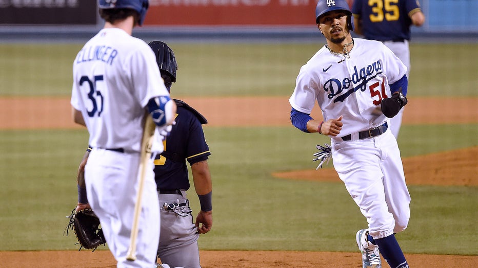 LOS ANGELES, CALIFORNIA - SEPTEMBER 30: Mookie Betts #50 of the Los Angeles Dodgers scores his run in front of Cody Bellinger #35 past Omar Narvaez #10 and Brent Suter #35 of the Milwaukee Brewers, from a Will Smith #16 walk, to take a 1-0 lead during the first inning in game one of the National League Wild Card Series at Dodger Stadium on September 30, 2020 in Los Angeles, California. (Photo by Harry How/Getty Images)