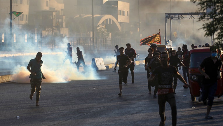 Iraqi protesters rush for cover from teargas fired by security forces during a demonstration against state corruption, failing public services, and unemployment, in the Iraqi capital Baghdad on October 5, 2019. - Renewed protests took place under live fire in Iraq's capital and the country's south Saturday as the government struggled to agree a response to days of rallies that have left nearly 100 dead. The largely spontaneous gatherings of demonstrators -- whose demands have evolved since they began on Tuesday from employment and better services to fundamental government change -- have swelled despite an internet blackout and overtures by the country's elite. Hours after a curfew in Baghdad was lifted on Saturday morning, dozens of protesters rallied around the oil ministry in the capital, facing live rounds fired in their direction, an AFP photographer said. (Photo by AHMAD AL-RUBAYE / AFP) (Photo by AHMAD AL-RUBAYE/AFP via Getty Images)